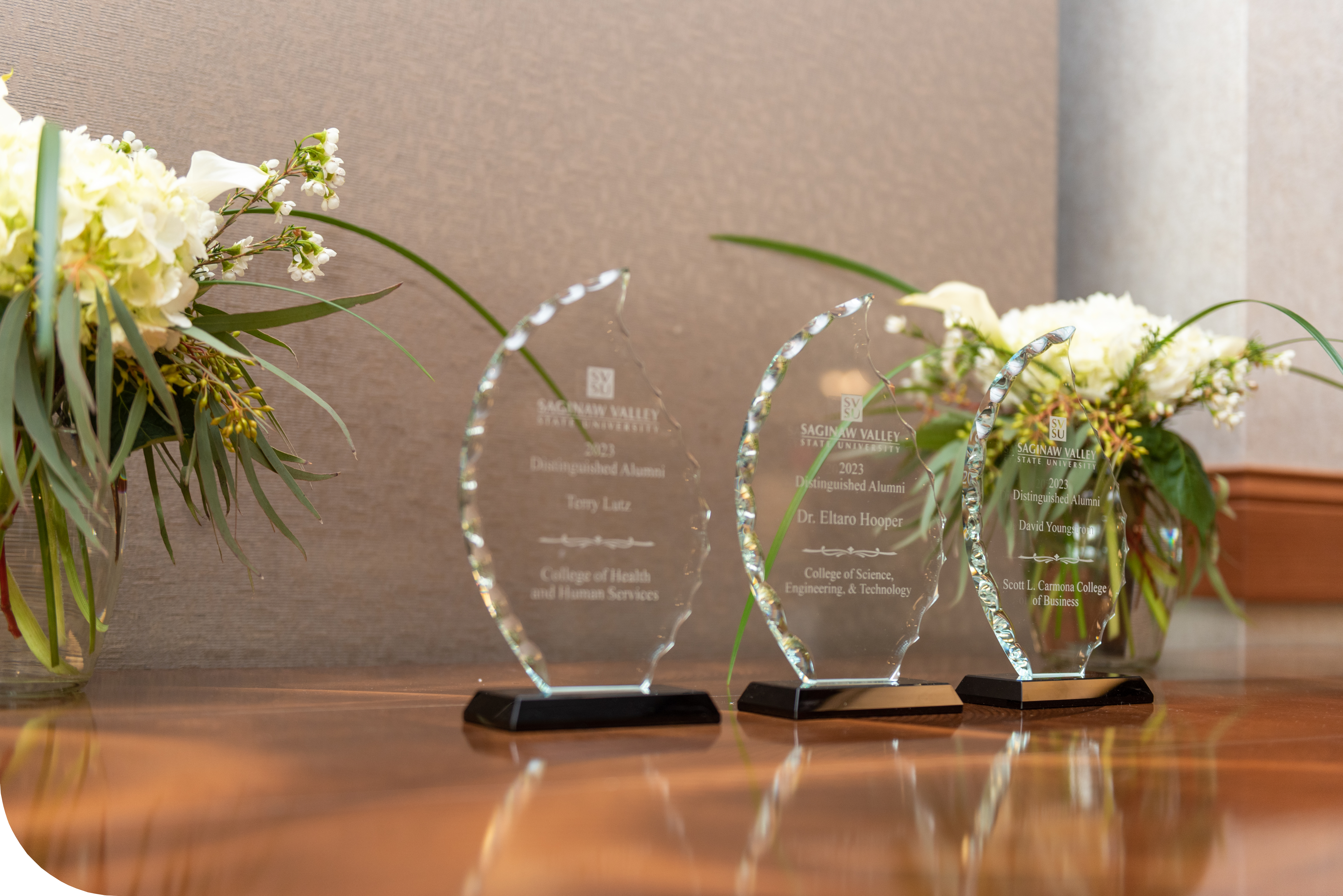 3 Distinguished Alumni Awards on a table surrounded by flowers
